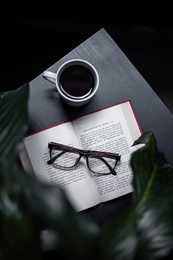 Eyeglasses On Opened Book Beside Cup Of Coffee On Table